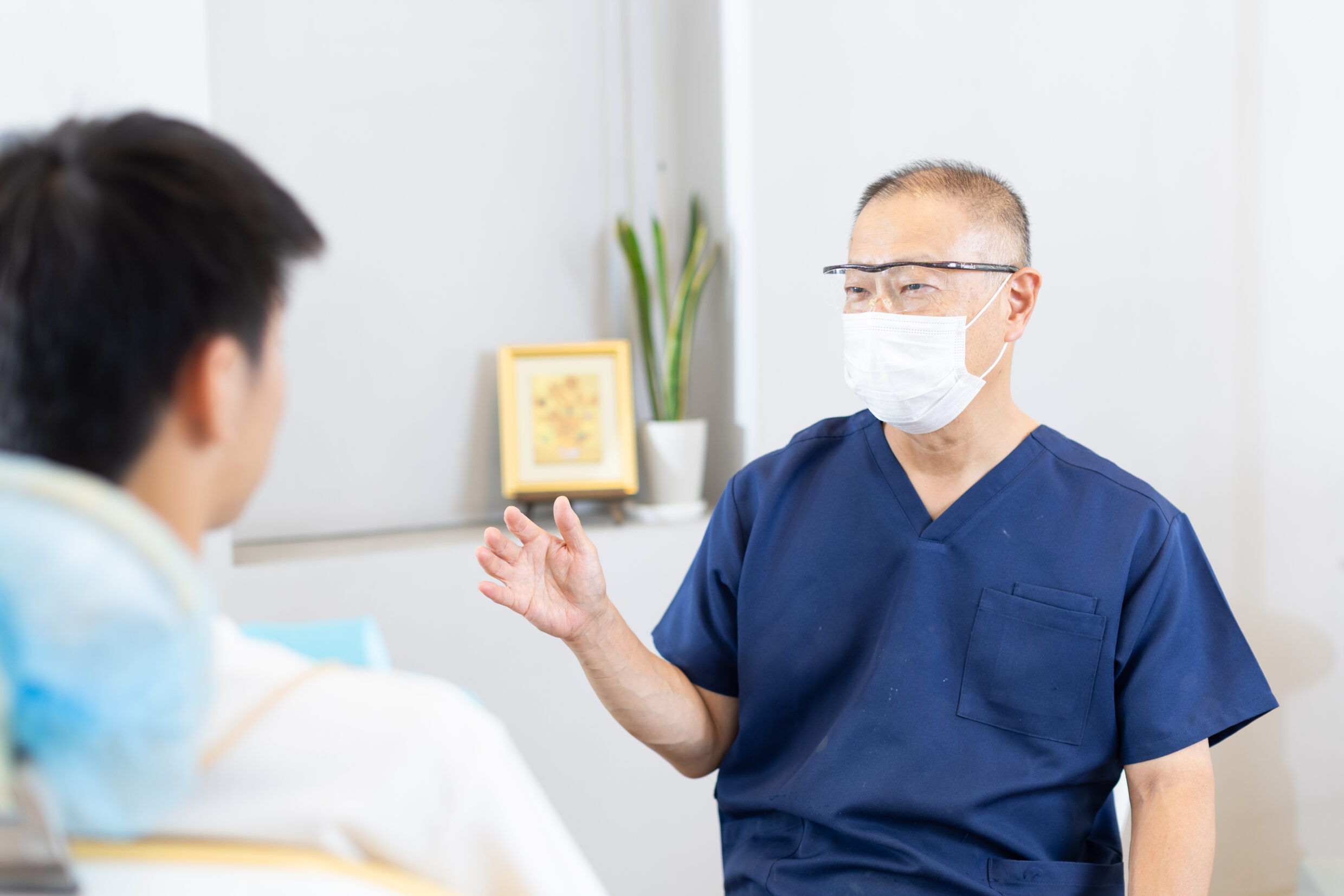 歯科医師が、手ぶりを交えながら患者と穏やかに会話をし、治療の仕上がりイメージや計画について説明を行っているカウンセリング風景。