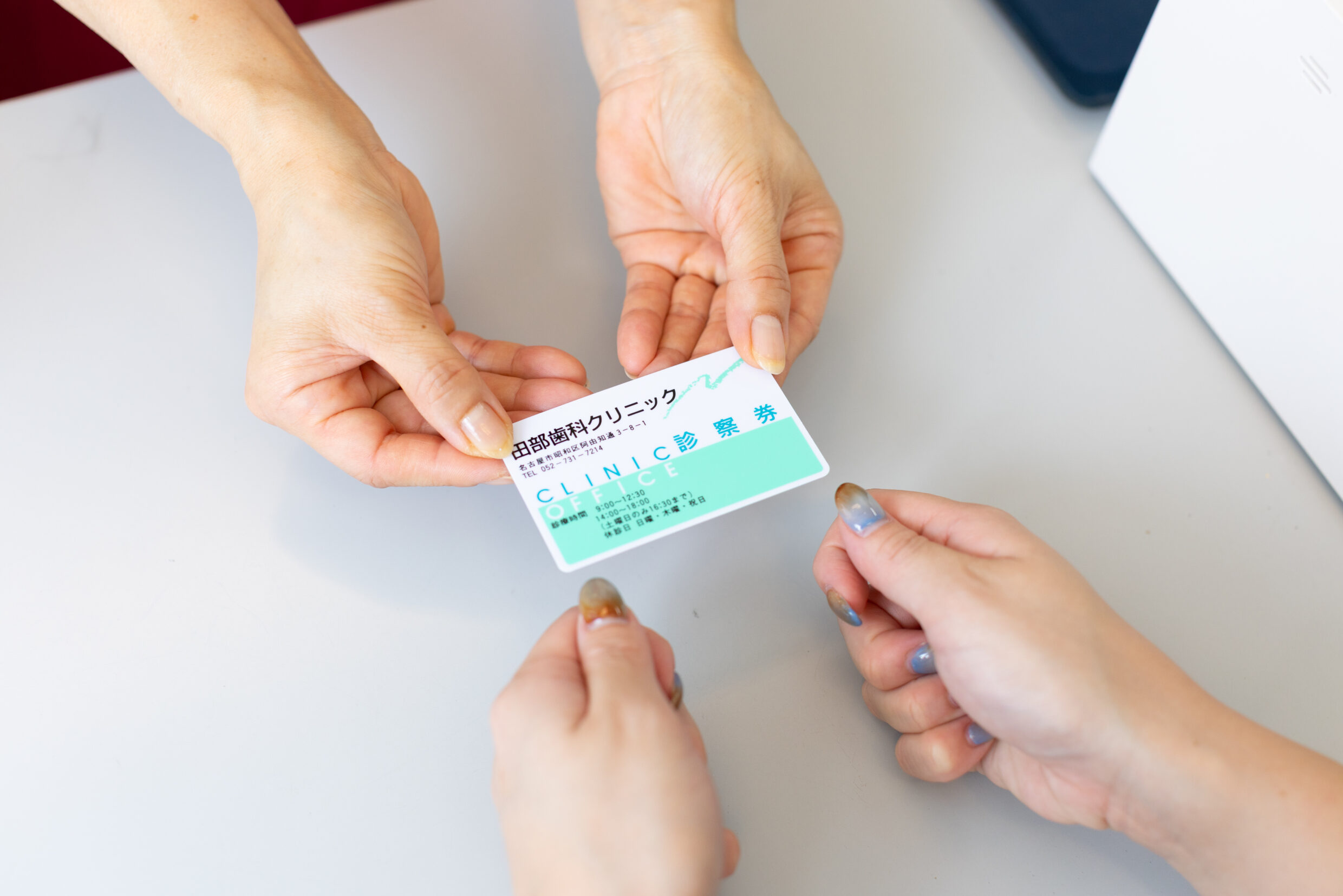 受付カウンターにて、スタッフが患者に歯科クリニックの診察券を手渡しで受け渡ししている手元の様子。